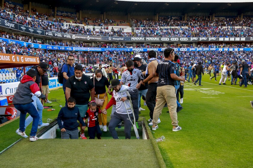 Fans go down stairs on the field at Corregidora Stadium in Queretaro, Mexico, Saturday to avoid a riot in the stands. 