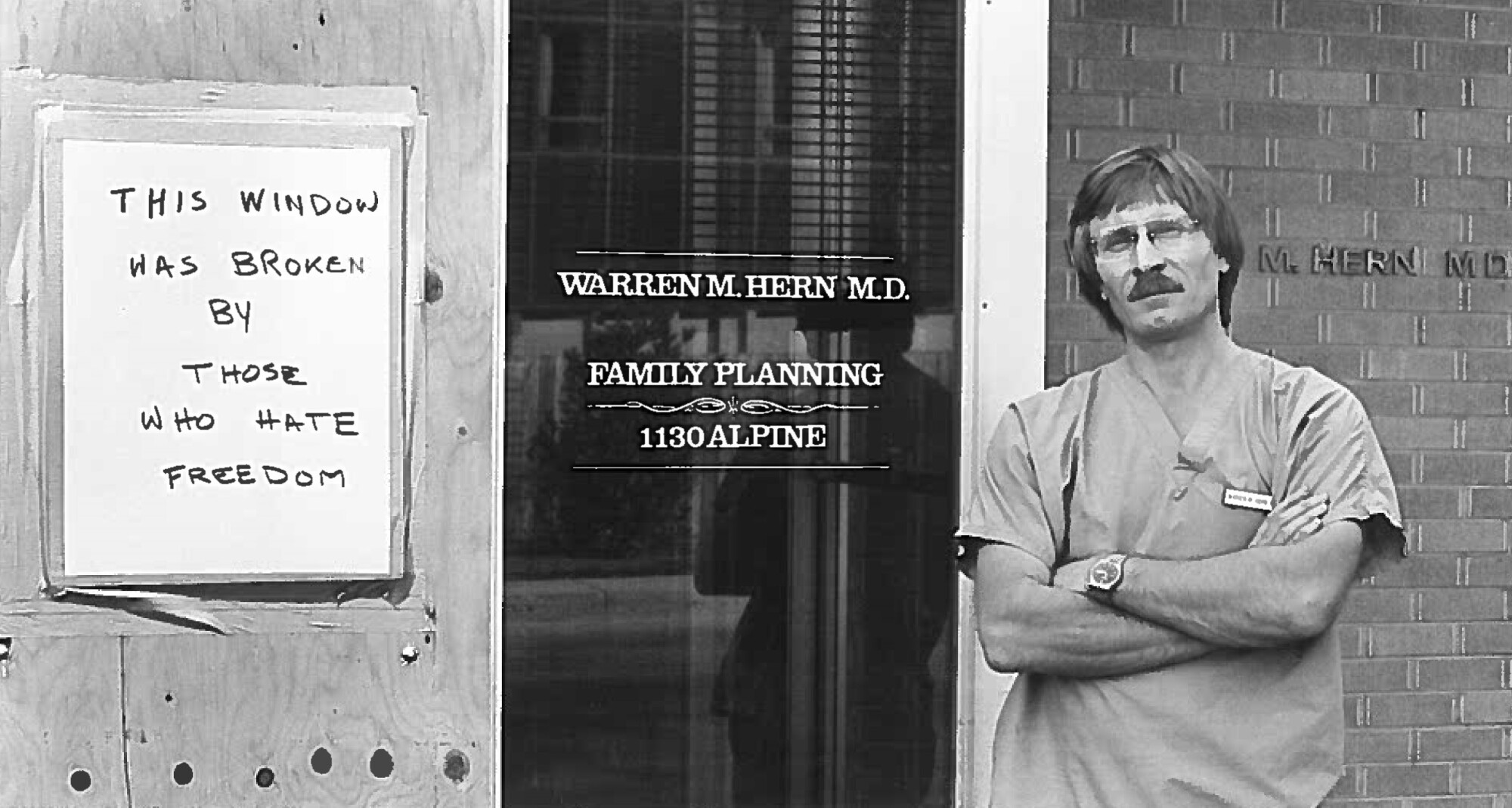 A doctor stands next to a boarded-up window with a sign: "This window was broken by those who hate freedom." 