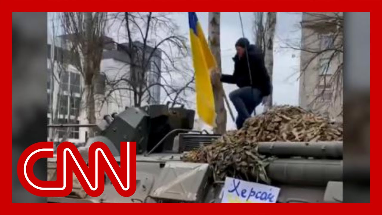 Man jumps on top of moving armored Russian vehicle while waving Ukrainian flag