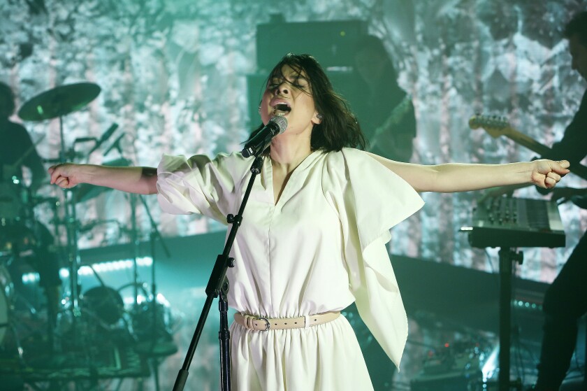 A female singer with outstretched arms performs onstage.