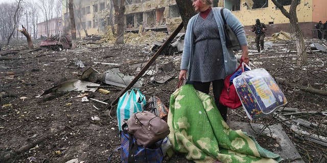 A woman walks outside the damaged by shelling maternity hospital in Mariupol, Ukraine, Wednesday, March 9, 2022. A Russian attack has severely damaged a maternity hospital in the besieged port city of Mariupol, Ukrainian officials say.