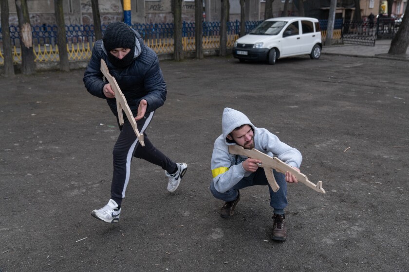 Two people hold wooden cutouts in the shape of rifles during a basic military training session