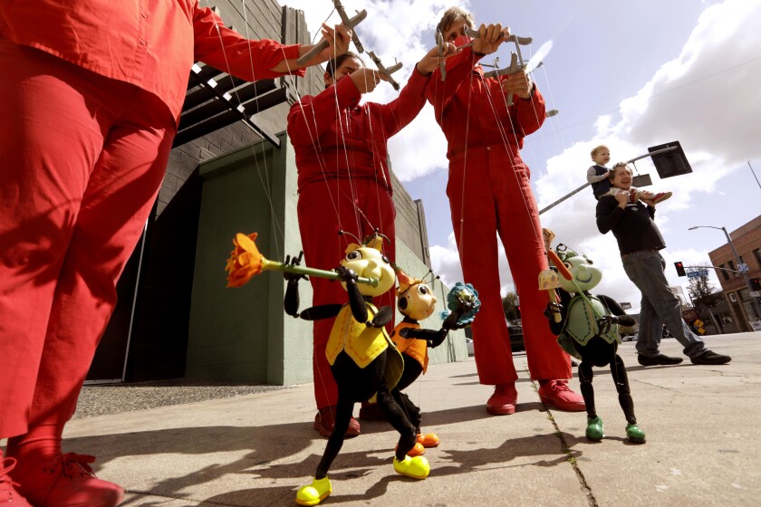 Puppeteers dressed all in red operate ladybug marionettes outside a theater.
