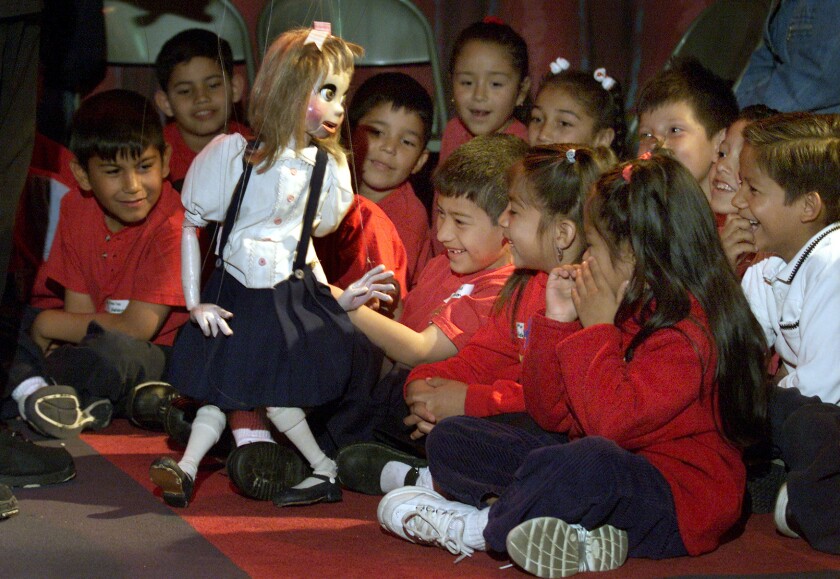 A crowd of kids giggles as a girl marionette entertains them.