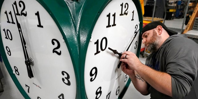 Clock technician Dan LaMoore adjusts clock hands on a large outdoor clock 