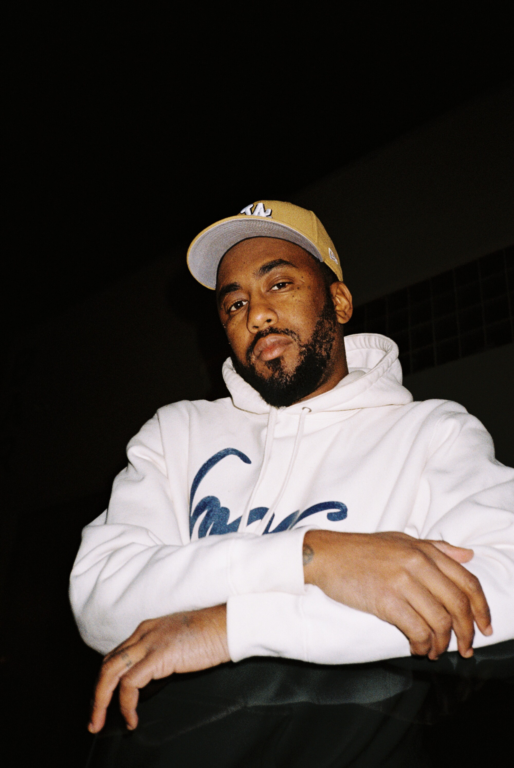 A man in a white hoodie and cap sits with folded arms.