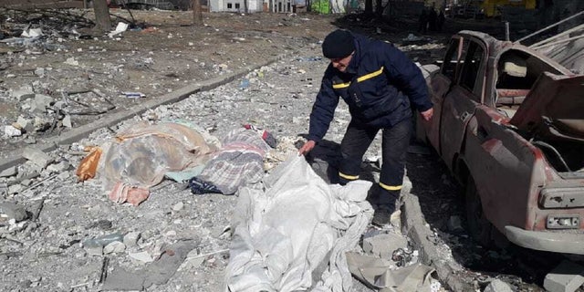 A man covers a dead body after residential buildings were hit by a Russian attack in Chernihiv, Ukraine.