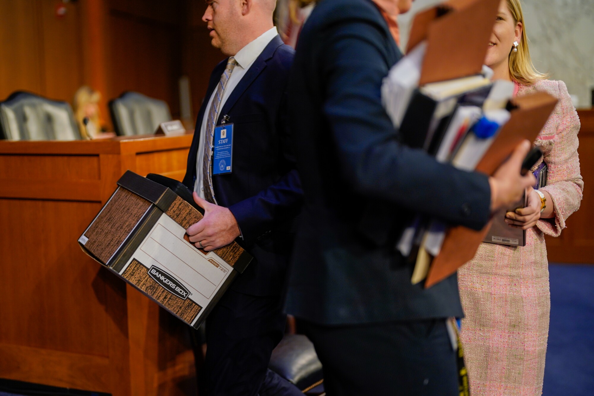 Congressional aides shuffle around the hearing room. 