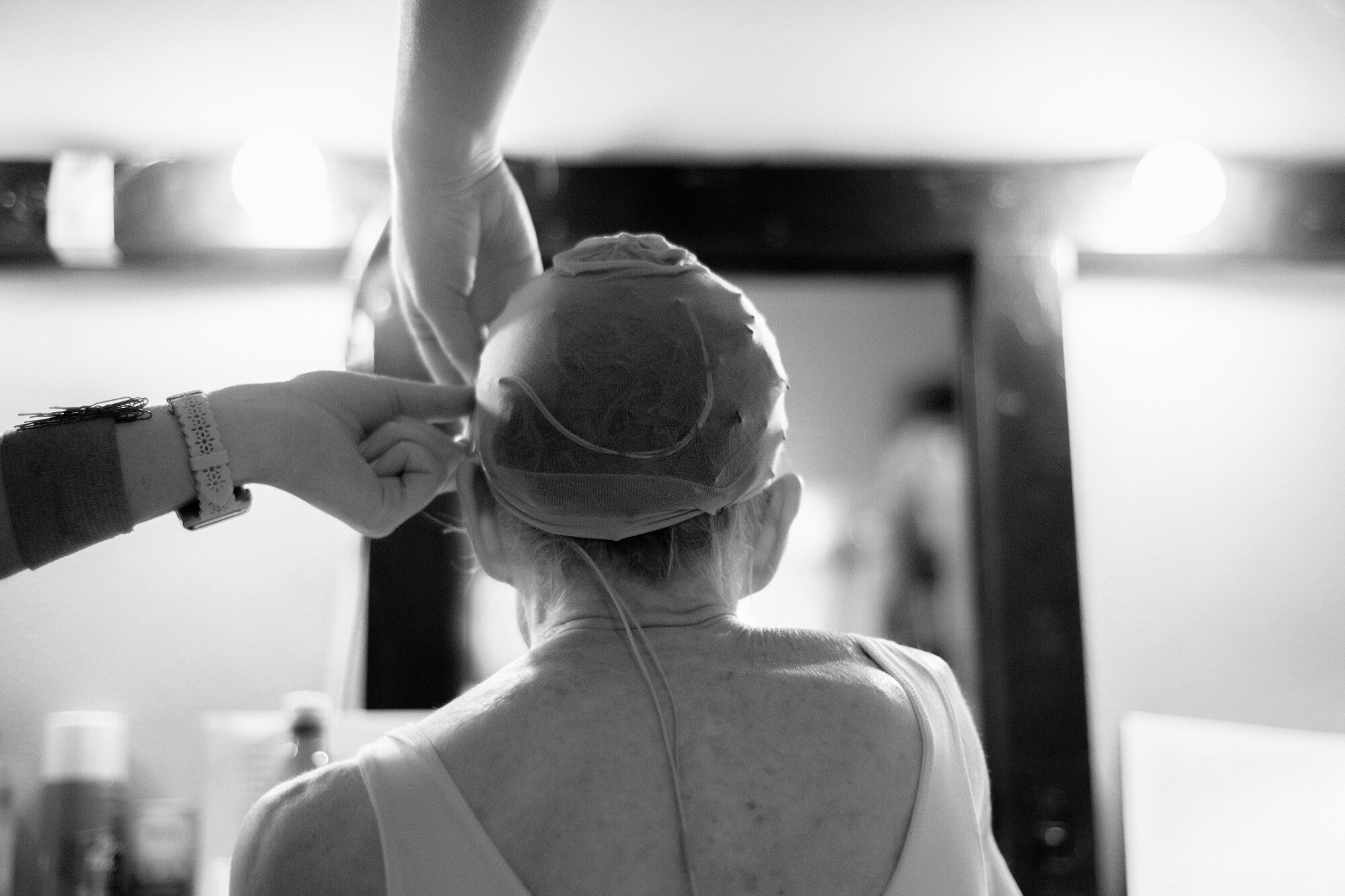 Hands install a microphone under a woman's wig cap.