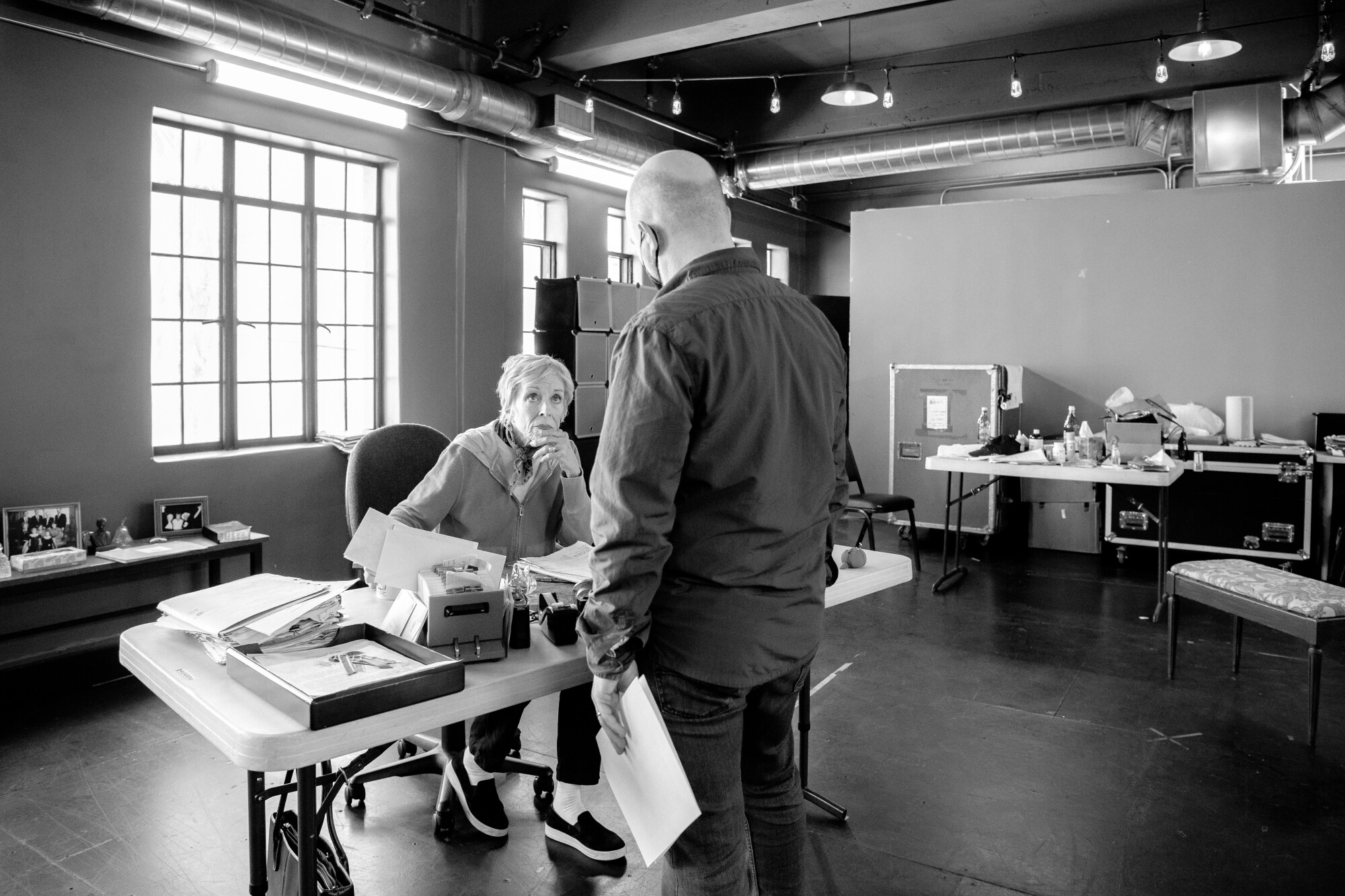 A standing man talks to a woman seated at a desk.