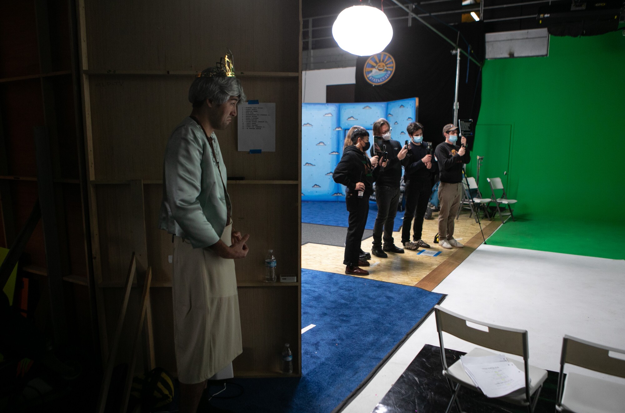 Dylan Adler watches from off-stage while crew members maneuver cameras and TeleprompTers.