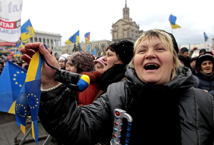 Protesters gather in a public square holding blue and yellow Ukrainian and EU flags.