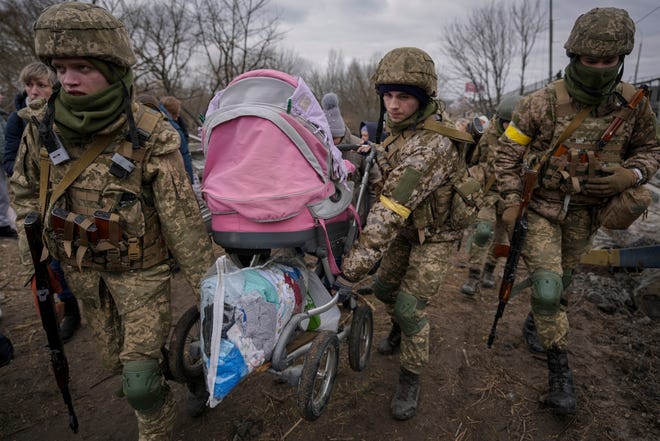 Ukrainian servicemen carry a baby stroller after crossing the Irpin River on an improvised path under a bridge that was destroyed by a Russian airstrike, while assisting people fleeing the town of Irpin, Ukraine, Saturday, March 5, 2022.