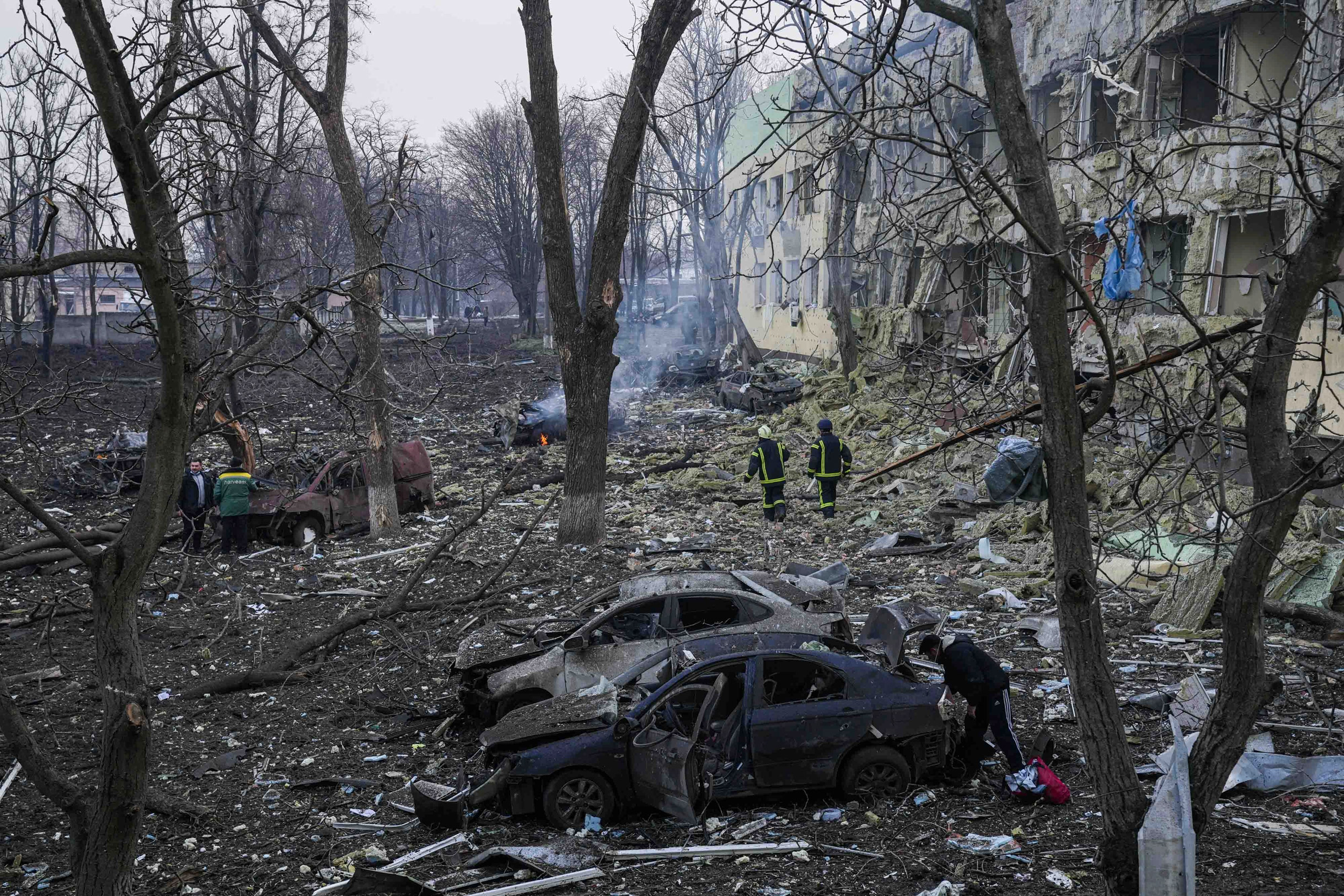 A scene of rubble, burnt-out cars and scorched trees outside a hospital building with blown out windows