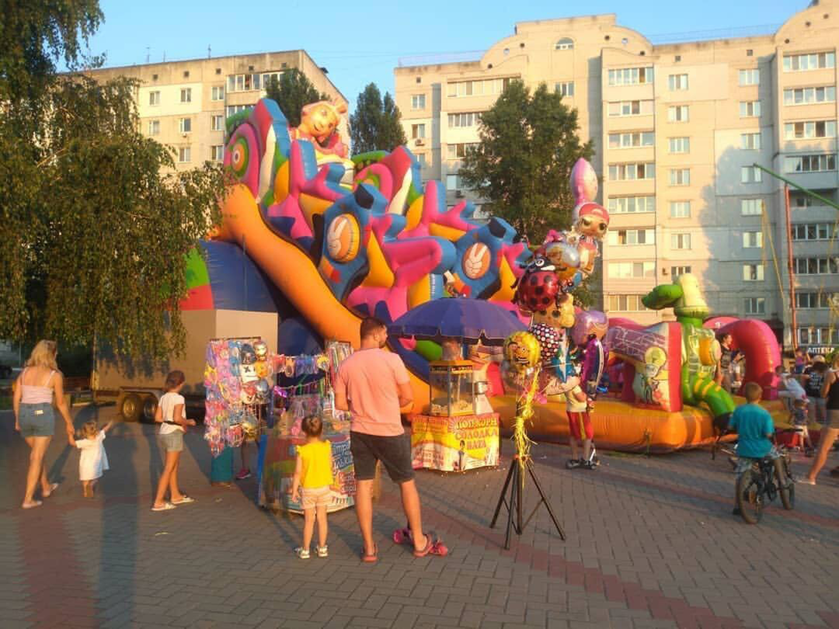 Popcorn and toy vendors by a huge colorful children’s inflatable in front of an apartment block