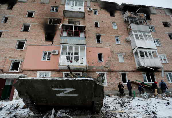 An armored vehicle with ‘Z’ markings in front of a burned apartment building.