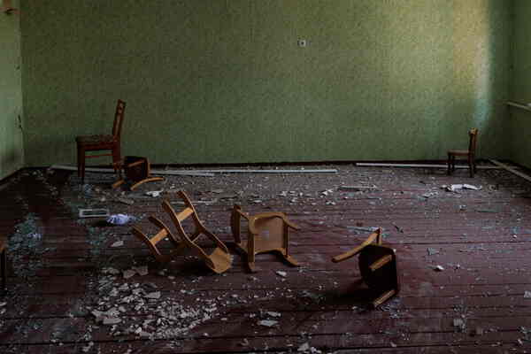 A green room with broken glass and damaged child-sized chairs.