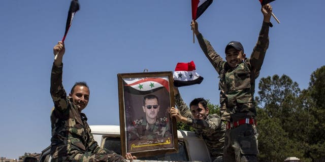 FILE - Syrian soldiers hold up Baath party flags and a portrait of Syrian President Bashar Assad. With its war on Ukraine now in its third week, Russian President Vladimir Putin on Friday, March 11, 2022, approved bringing in volunteer fighters from the Middle East into the conflict. 