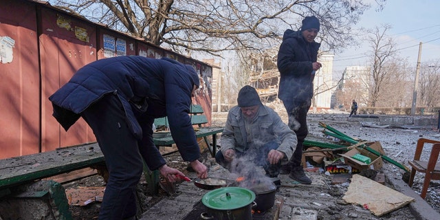 Men cook a meal in a street in Mariupol, Ukraine, Sunday, March 13, 2022. The surrounded southern city of Mariupol, where the war has produced some of the greatest human suffering, remained cut off despite earlier talks on creating aid or evacuation convoys. (AP Photo/Evgeniy Maloletka)