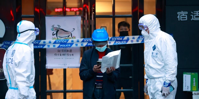 A delivery man walks by police officers with protective suit outside of a hotel in Shanghai, China, on March 15, 2022. 