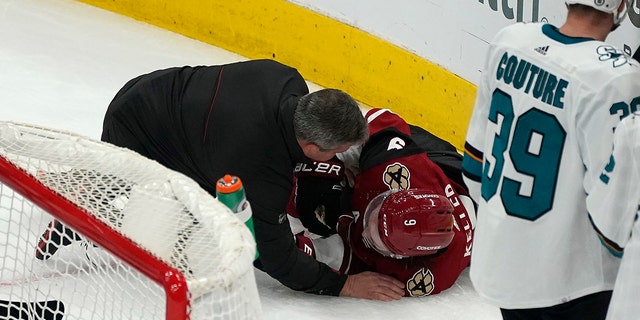 A trainer attends to Arizona Coyotes' Clayton Keller (9), who collided against the boards during the third period of the team's NHL hockey game against the San Jose Sharks, Wednesday, March 30, 2022, in Glendale, Arizona.