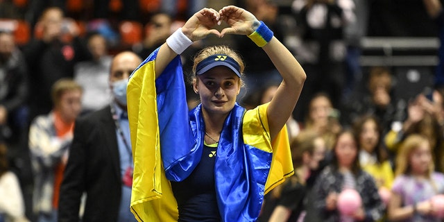 Ukraine's Dayana Yastremska, wrapped in the Ukrainian national flag, reacts at the end of the WTA 6eme Sens Open semi-final tennis match against Romania's Sorana Cirstea in Lyon, on March 5, 2022.