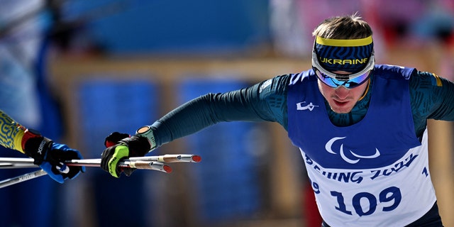 Ukraines Dmytro Suiarko grabs his poles from his guide in the mens sprint vision impaired biathlon event on March 5, 2022, at the Zhangjiakou National Biathlon Centre, during the Beijing 2022 Winter Paralympic Games.