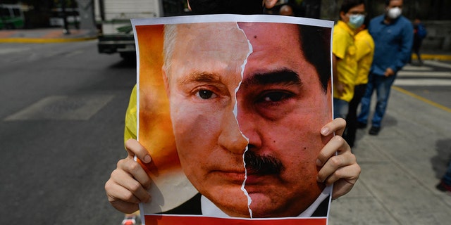 An activist member of opposition party Primero Justicia holds a placard showing the face of Russian President Vladimir Putin and Venezuelan President Nicolas Maduro during a protest against the Russian invasion in Ukraine, in Caracas on March 4, 2022. 