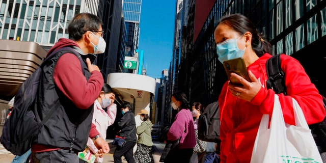 People wearing face masks walk across a main street at a downtown street in Hong Kong, Wednesday, March 9, 2022. 