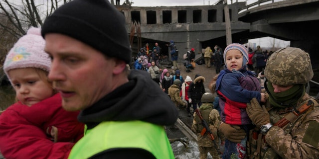 A Ukrainian serviceman holds a baby while crossing the Irpin River on an improvised path under a bridge that was destroyed by a Russian airstrike, on March 5, 2022.