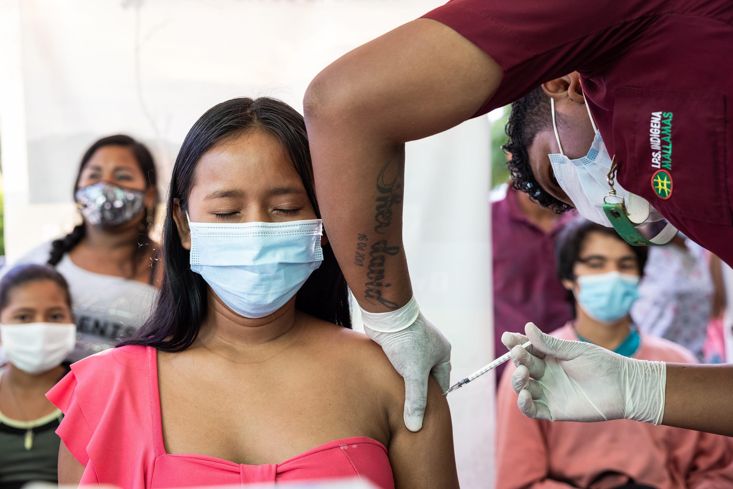 Romario Mujica applies a vaccine to a young Indigenous woman who closes her eyes to avoid seeing the needle.