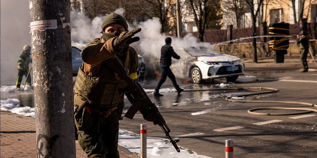 Ukrainian soldiers take positions outside a military facility as two cars burn in a street in Kyiv, Ukraine, Saturday, Feb. 26, 2022.