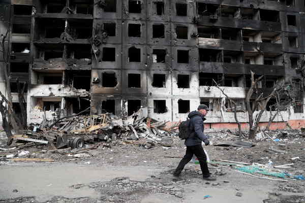 A man walks by a shell of rectangle burnt windows.