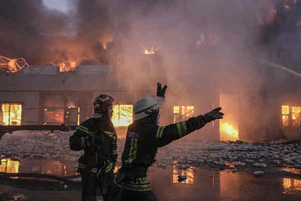 Firefighters gesture at a burning building.