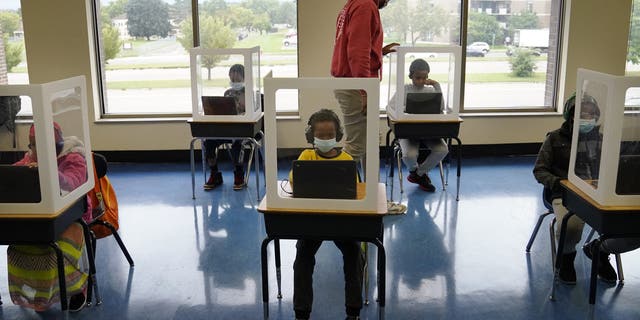 MINNEAPOLIS, MN,- SEPTEMBER 8 - It was back to school for some students at Harvest Best Academy Tuesday in Minneapolis, but with masks, plastic barriers and other new precautions in the era of COVID-19. Here, para professional Jaevon Walton, middle, reminded a student to wear his face mask in a learning pod of 2nd through 7th graders, Tuesday, Sept. 8, 2020, in Minneapolis. 