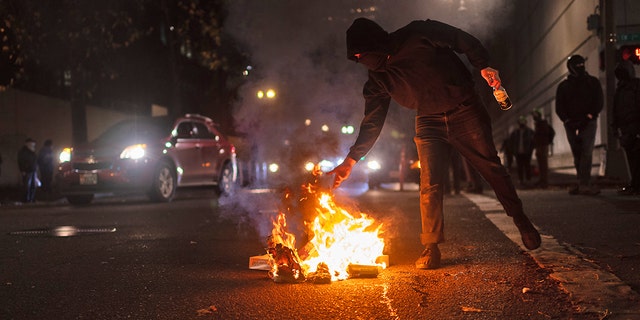 A protester feeds a small fire near the south entrance of the Justice Center after a riot was declared during a protest to decry the verdict in the Kyle Rittenhouse Trial. Portland, Oregon, USA, November 19th, 2021.