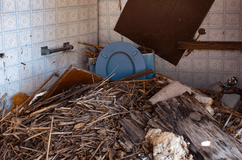 Wooden debris piled up in a bathroom nearly covering up a light blue toilet.