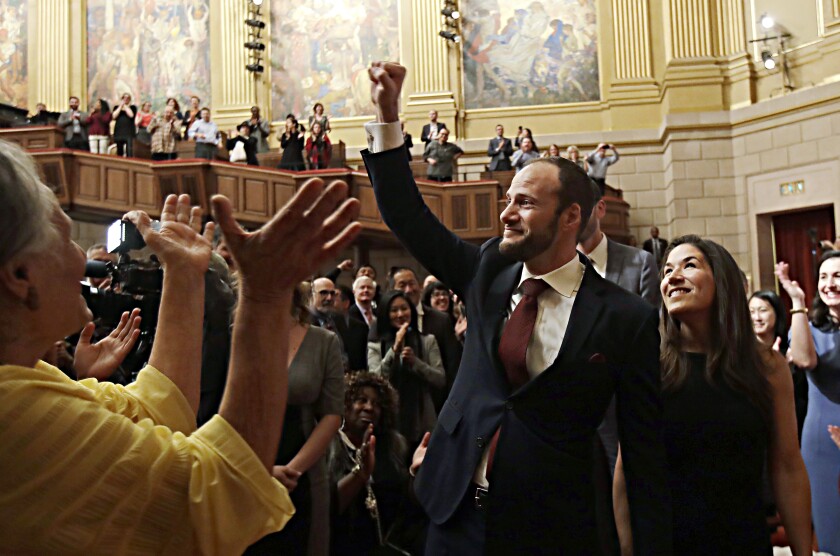 A man raises his right arm in a chamber of cheering people.