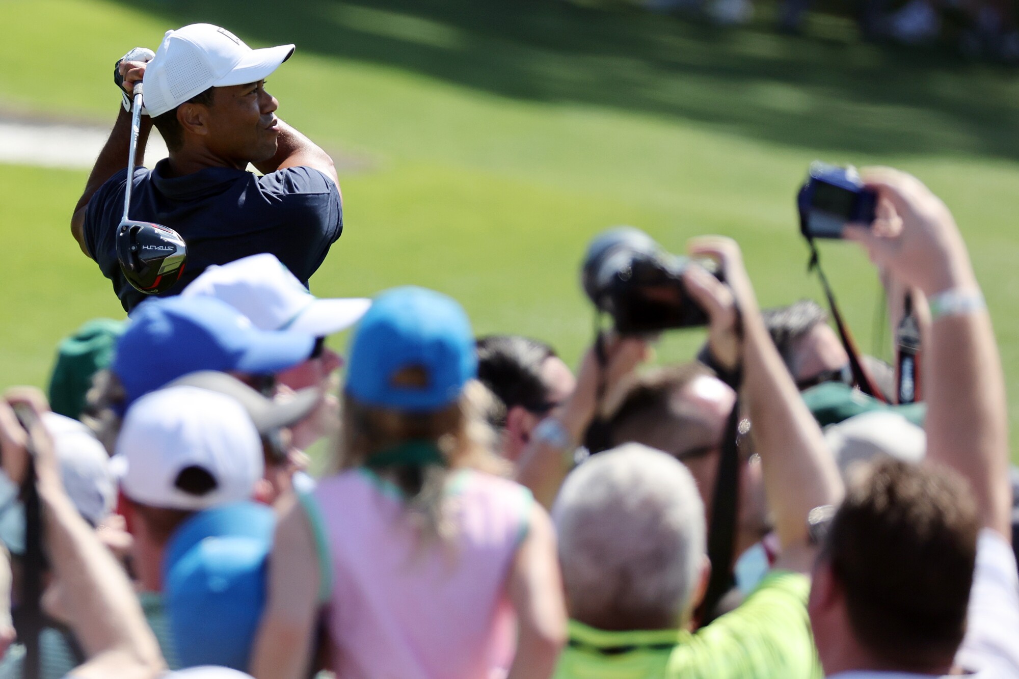 People take photos as Tiger Woods swings a club