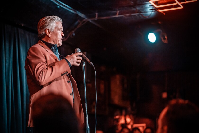 A man in an orange suit jacket performs stand-up