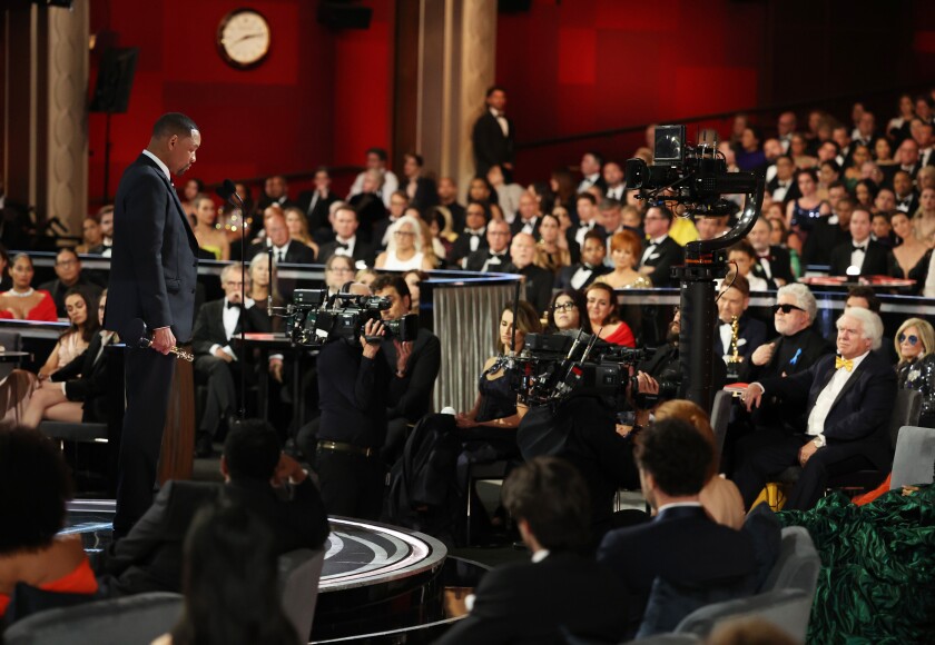 A man in a tux onstage addressing a theater