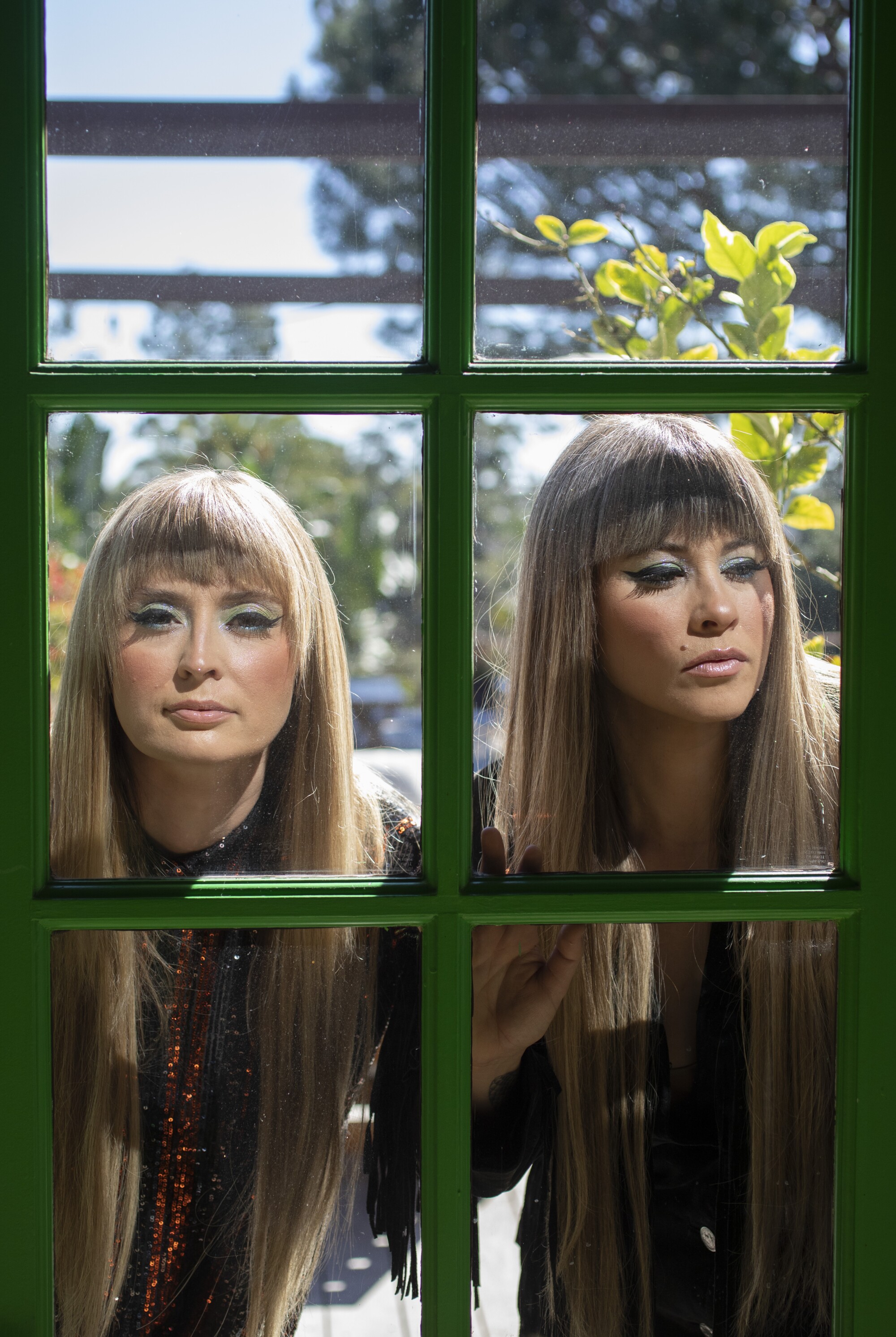 Two women with matching hair styles look through a window