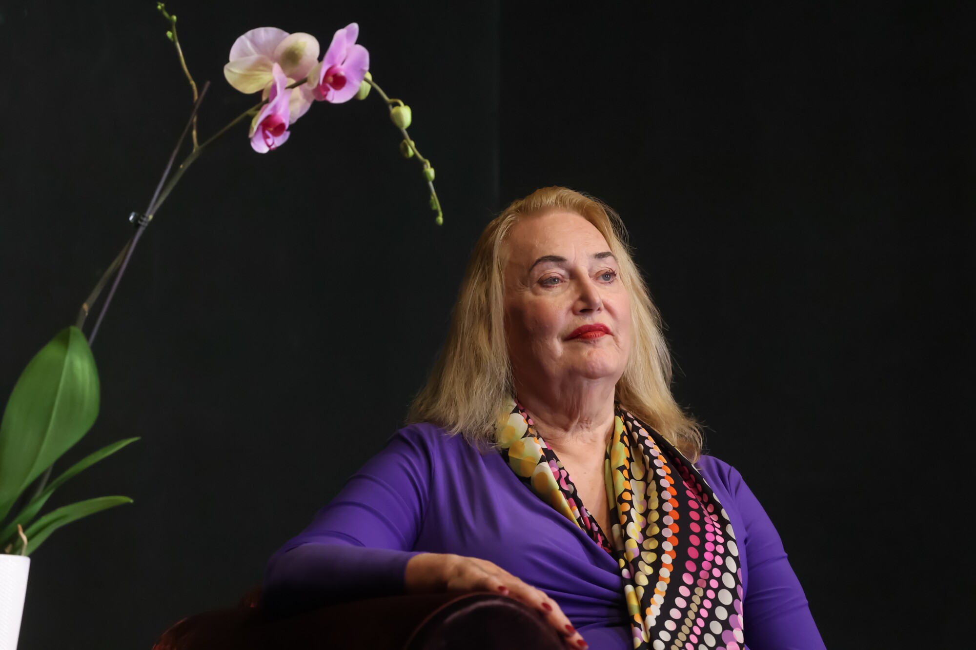 A woman sits by a plant.