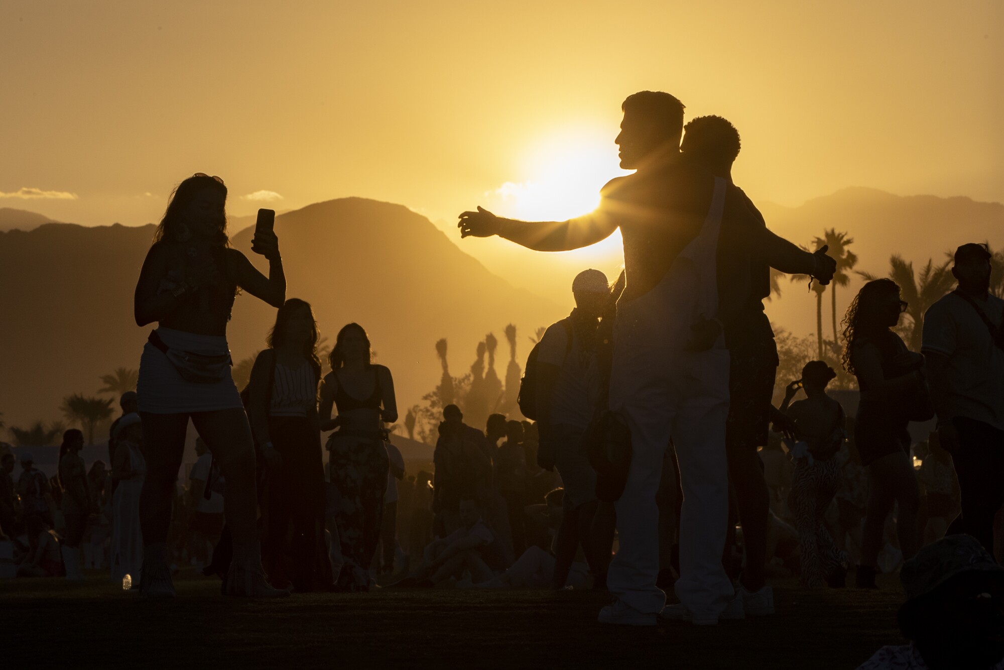 People are silhouetted as the sun sets on the first day of the 2022 Coachella Valley Music and Arts Festival.