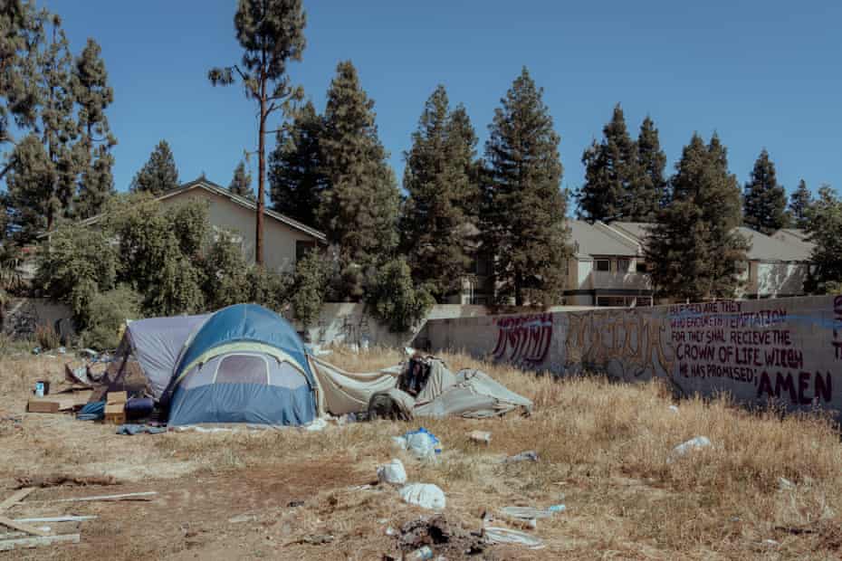 A blue tent in a dry field, homes in the background