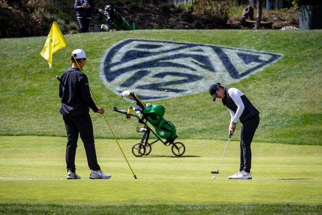 Oregon’s Hsin-Yu Lu, left, holds the flag as Tze-Han Lin putts on the fifth hole during a practice round at the Eugene Country Club on Friday.