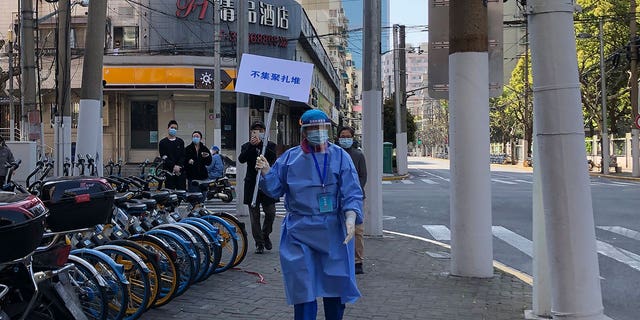 A worker in protective gear holds a sign which reads "Do not crowd" during a mass testing day for residents in a lockdown area in the Jingan district of western Shanghai