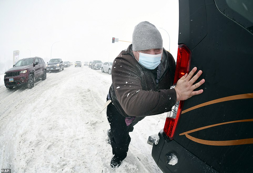 Matt Mittelstaedt, a driver for Missouri Slope Lutheran Care Center, pushes as a Good Samaritan tows the large passenger van he was driving when it got stuck in the snow at the intersection of State Street and Divide in Bismarck, ND on Tuesday