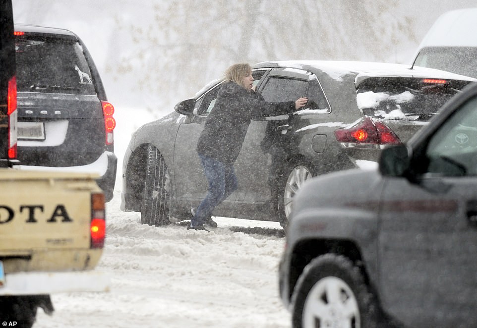 A woman tries to push a stuck car in the snow at the intersection of State Street and Divide Avenue in Bismarck ND on Tuesday