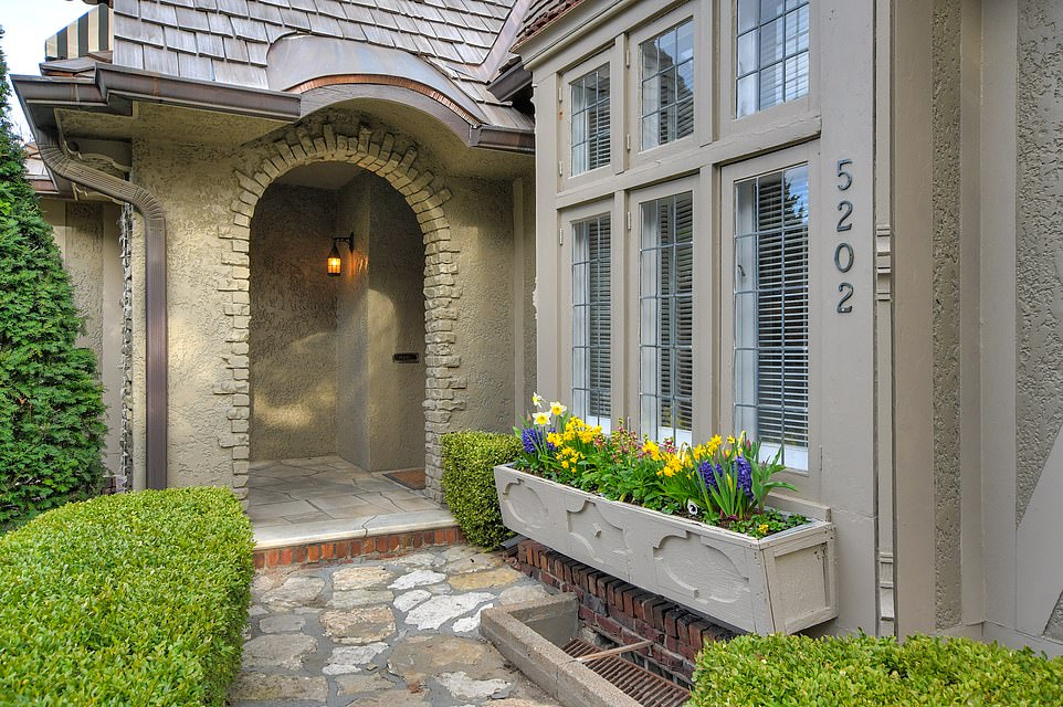 The home features a flower basket on the windowsill next to the house number and the front path is decorated with luscious greenery